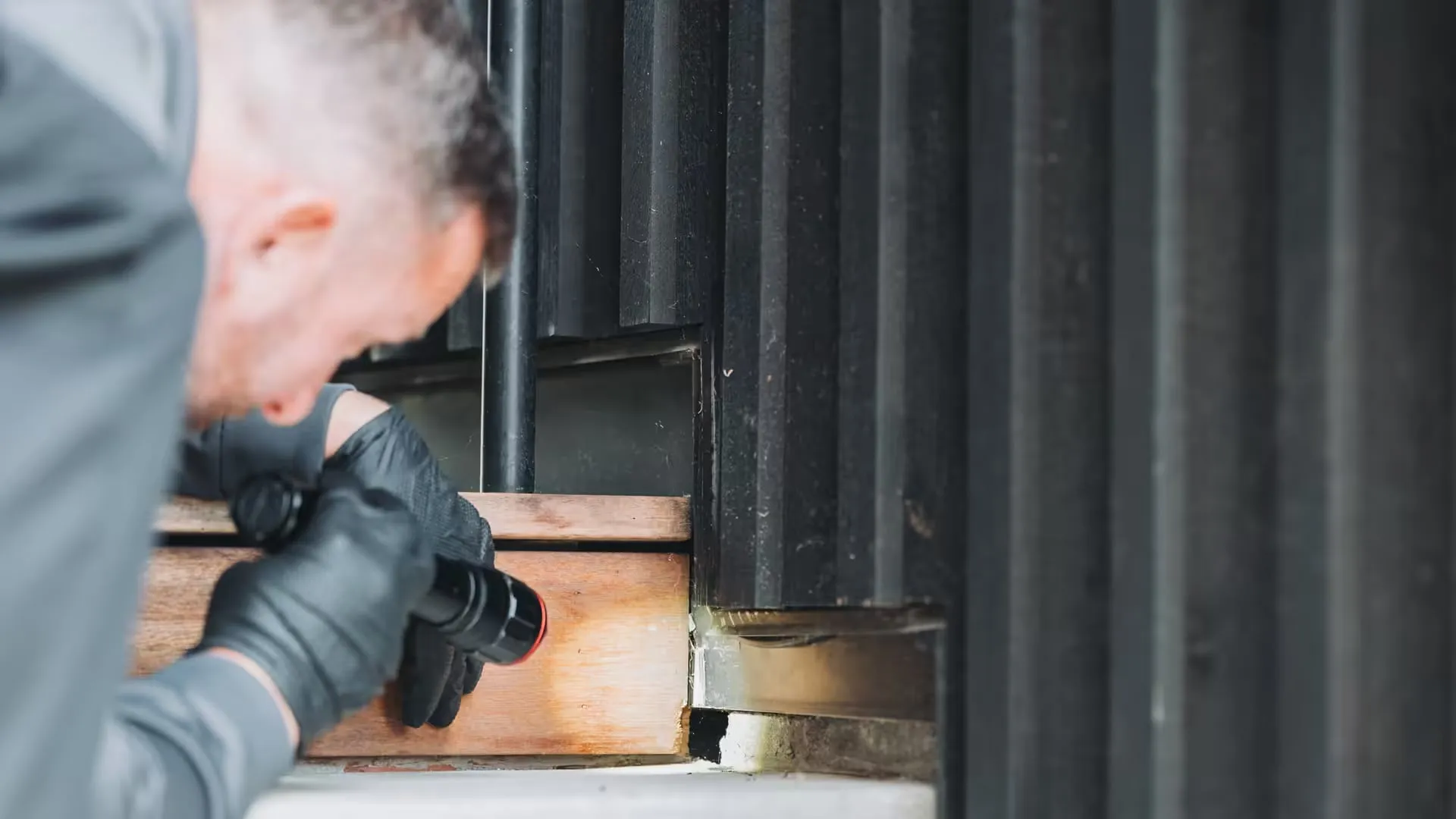 An A&A technician inspecting the base of a home's siding for rodent activity
