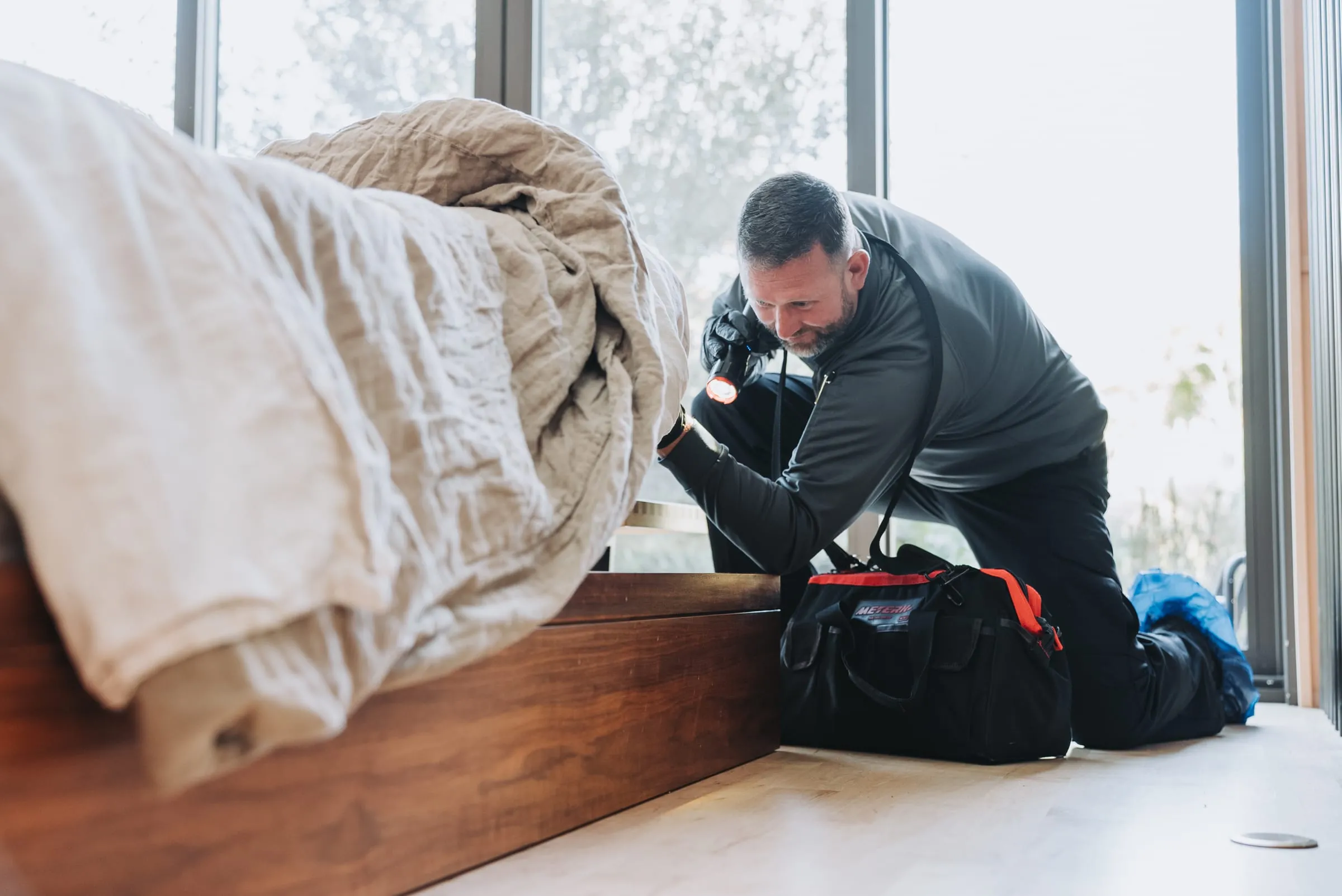 An A&A technician checking the edge of a bed frame with a flashlight