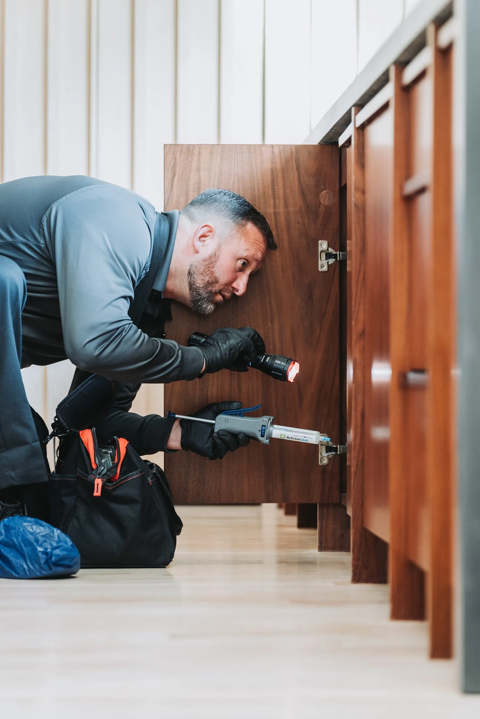 An A&A technician baiting for ants beneath a kitchen cabinet