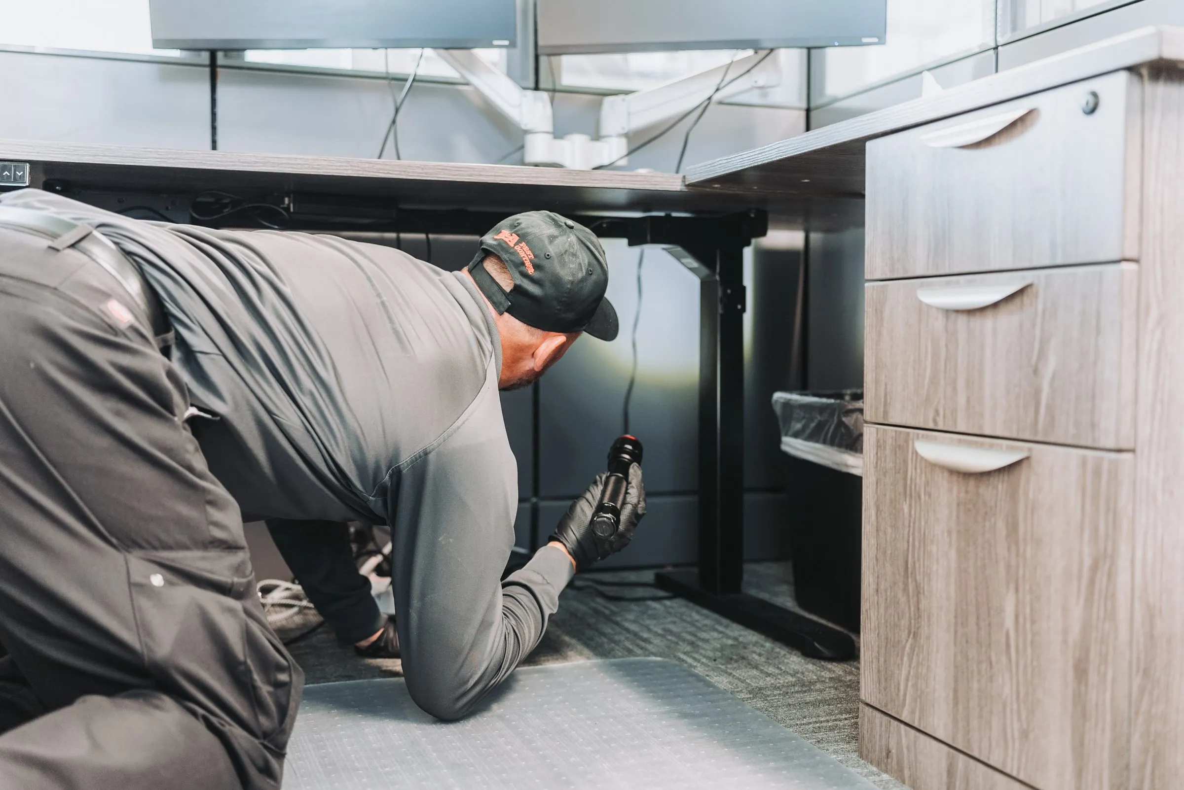 An A&A technician inspecting under a desk with a flashlight