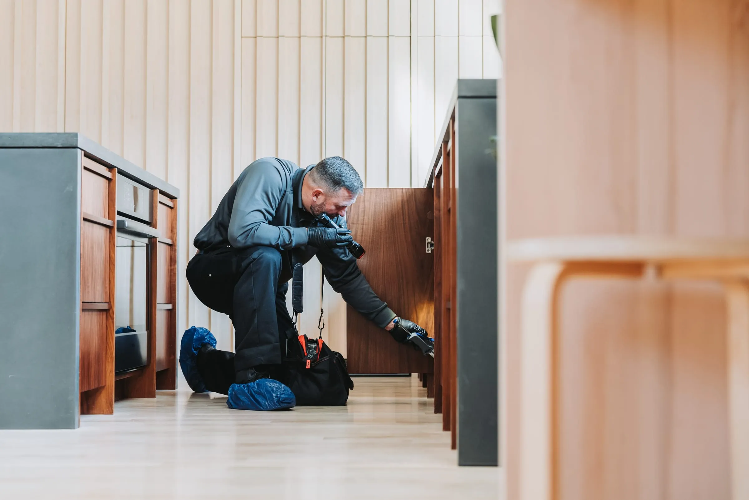 An A&A technician kneeling to bait along the base of kitchen cabinets
