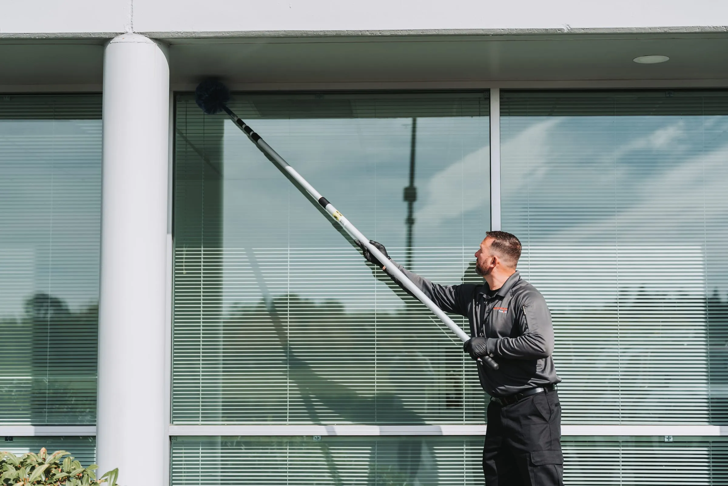 An A&A technician clearing webs from a building's eaves with an extension pole