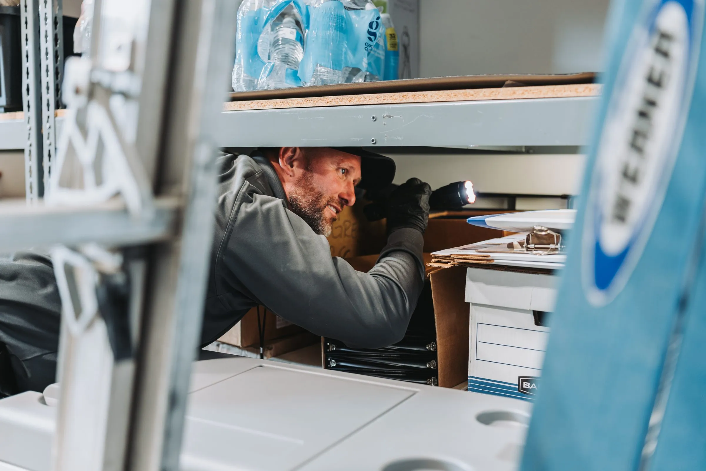 An A&A technician inspecting beneath shelving in a commercial storeroom