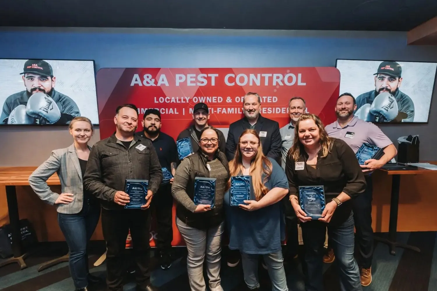 A&A team members holding award plaques in front of the company's screens at an awards event