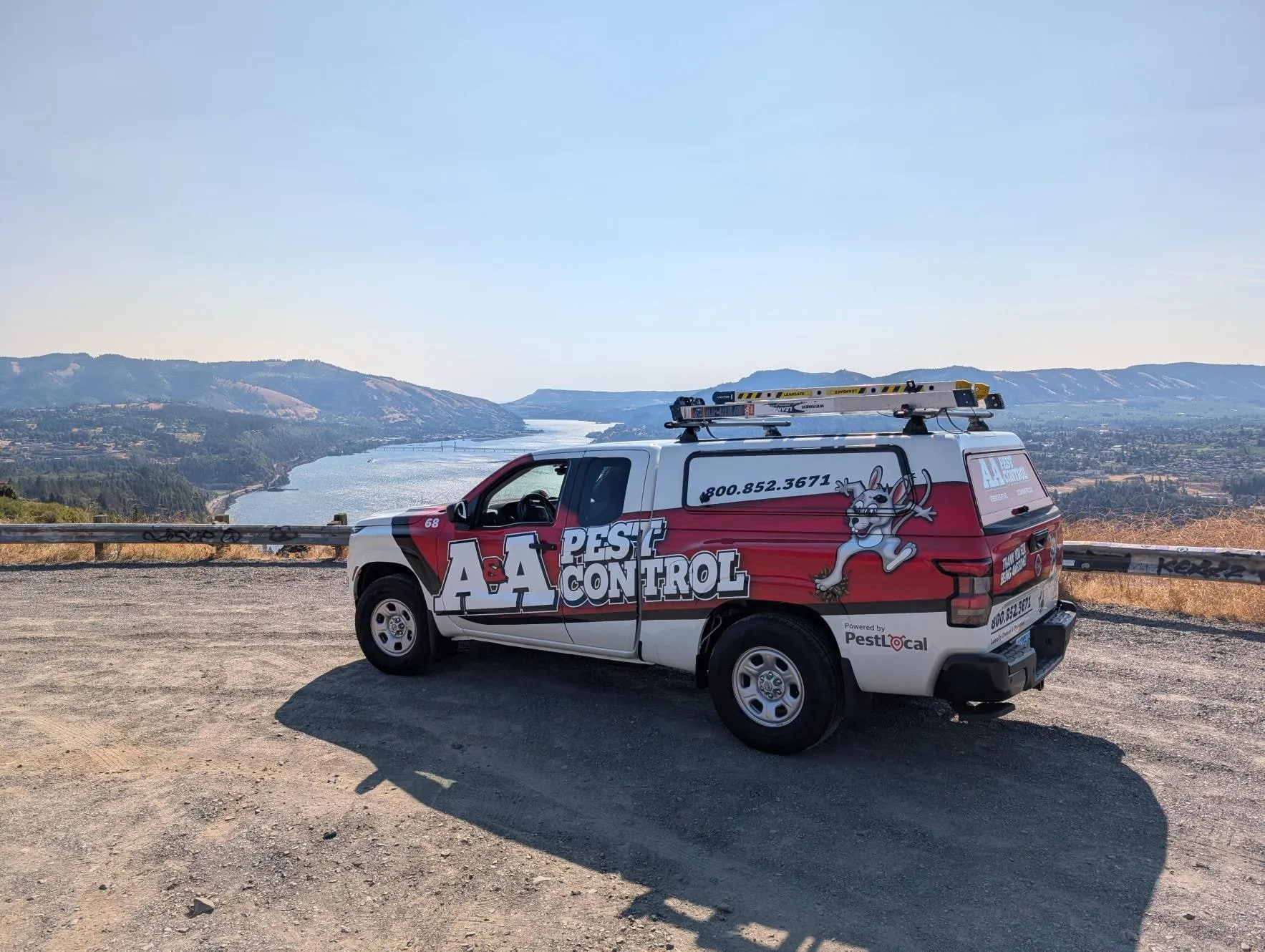 An A&A Pest Control truck parked on a gravel overlook above a wide river valley