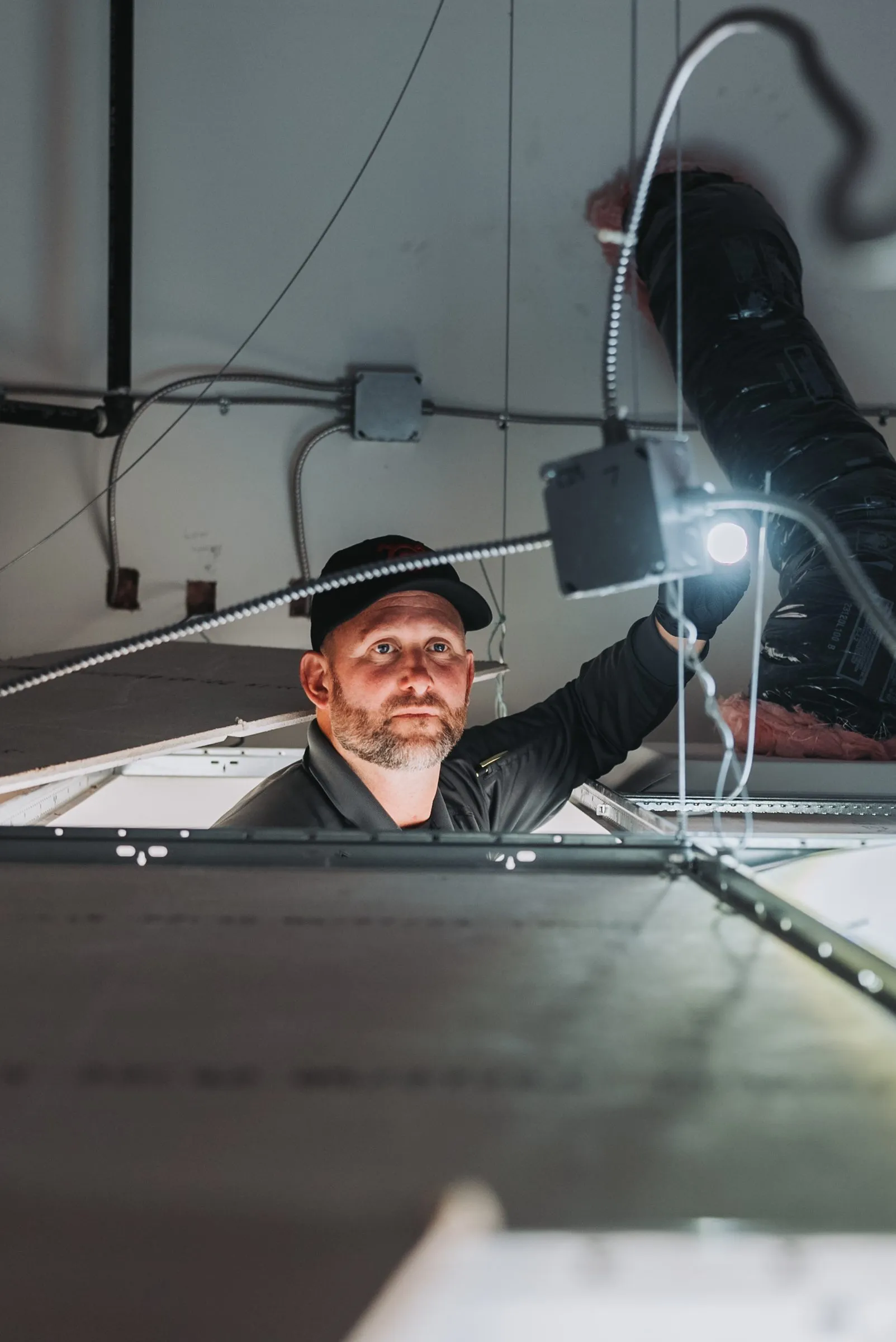 An A&A technician inspecting a commercial ceiling space with a flashlight