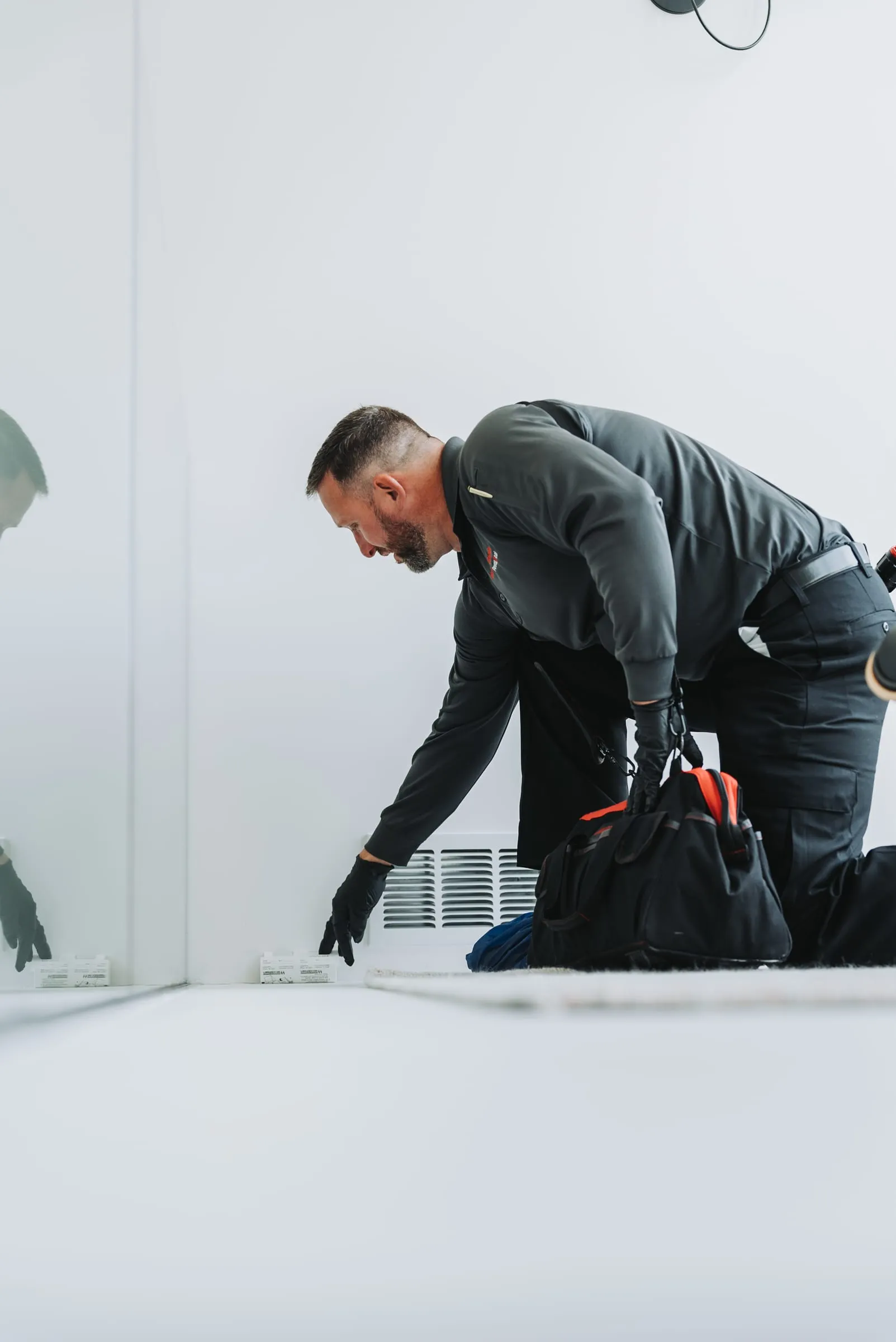 An A&A technician kneeling to place an insect monitor along a baseboard