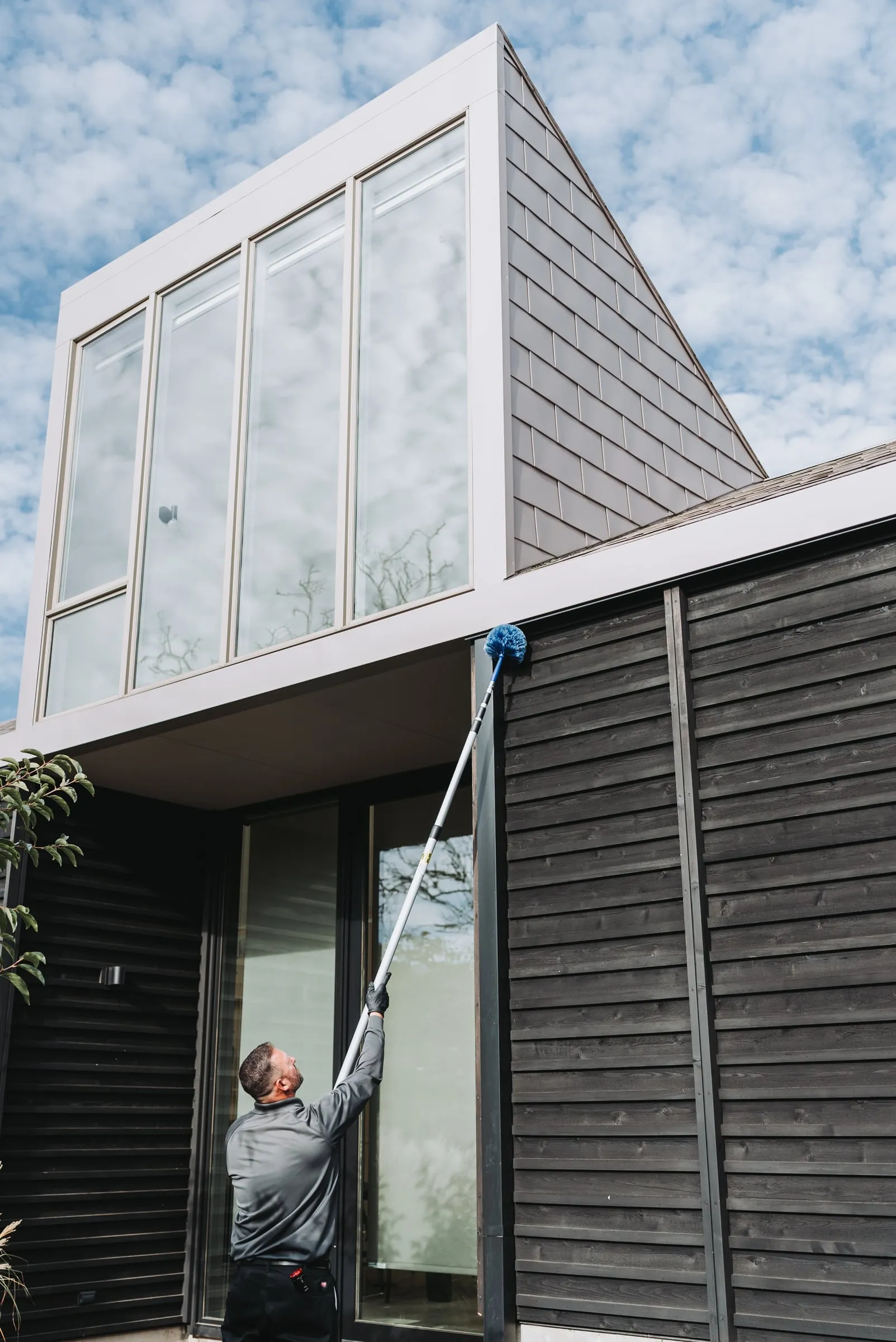 An A&A technician reaching up with an extension pole and web brush to clear webs from under a home's eave