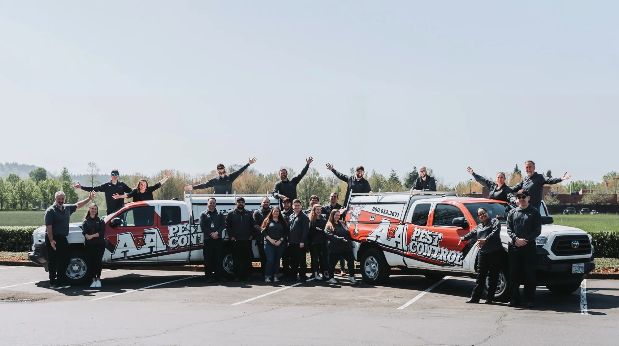 The A&A Pest Control team lined up in front of two service trucks with their arms out wide