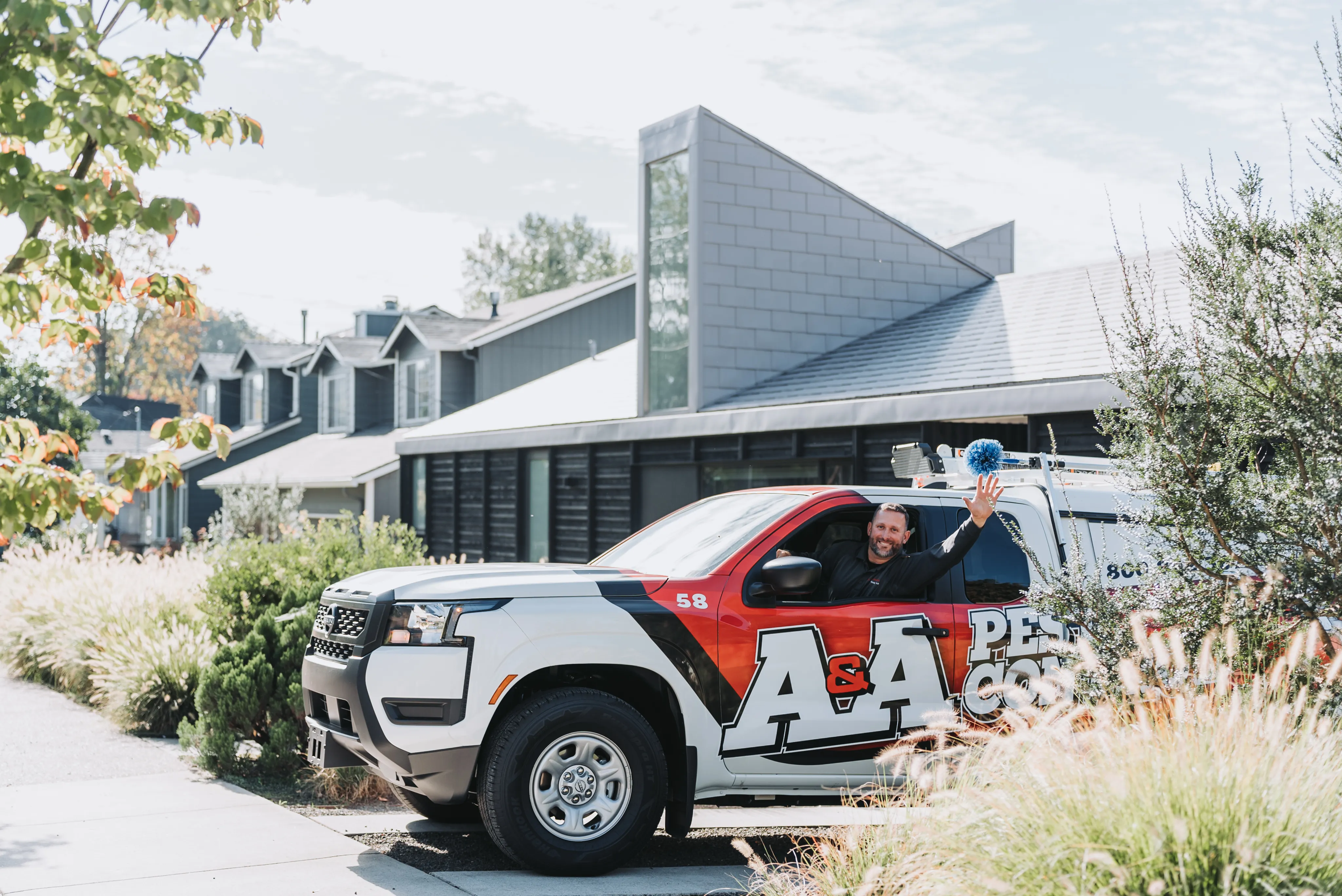 An A&A Pest Control technician waving from the window of his service truck outside a customer's home