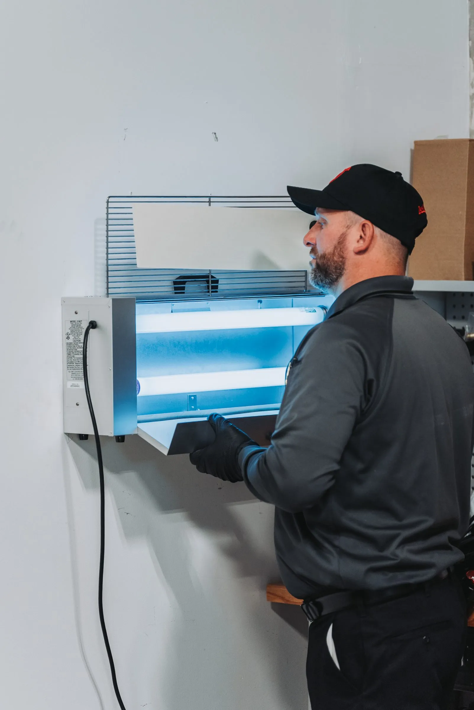 An A&A technician servicing a wall-mounted fly light in a commercial space